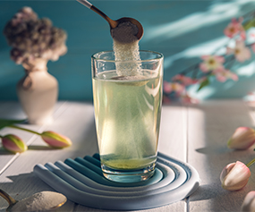 Glass with green liquid and floral elements symbolizing natural ingredients in hydrolyzed proteins for skincare